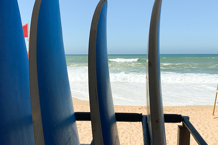 Surfboards lined up on a sandy beach with ocean waves in the bac
