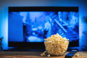 A glass bowl of popcorn and remote control in the background the TV works, a Food & Drink Photo by Budarinphoto