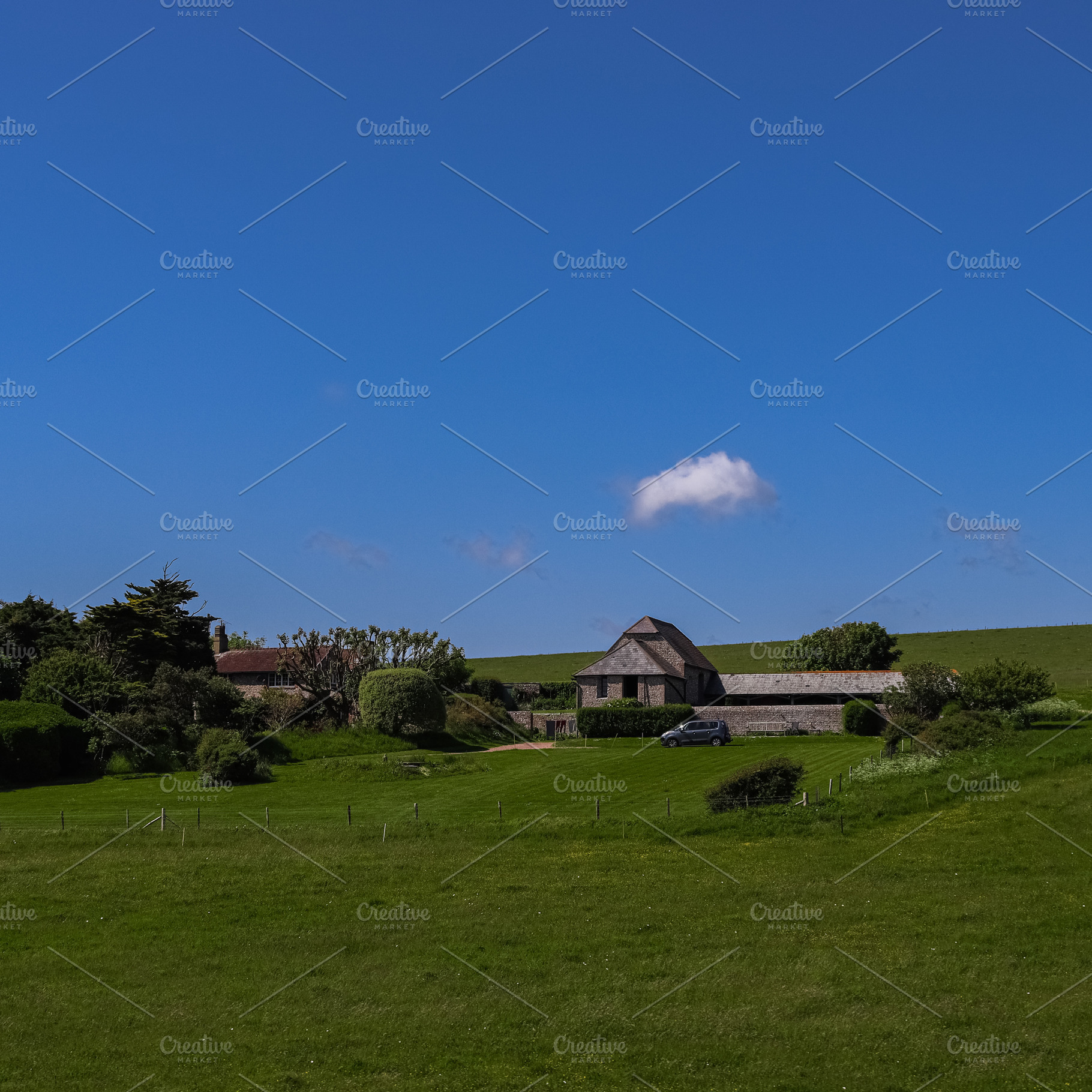 Rural landscape with a traditional stone barn, green grass fields, and blue sky, a Photo by Studio ANNA