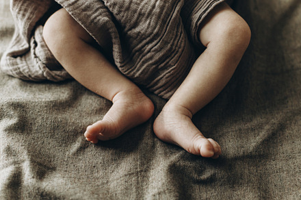 Adorable little baby feet close up in blanket on brown bed. Adop