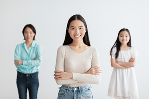 Young Asian woman with mature mother and cute daughter posing with crossed arms, a Photo by Prostock-Studio