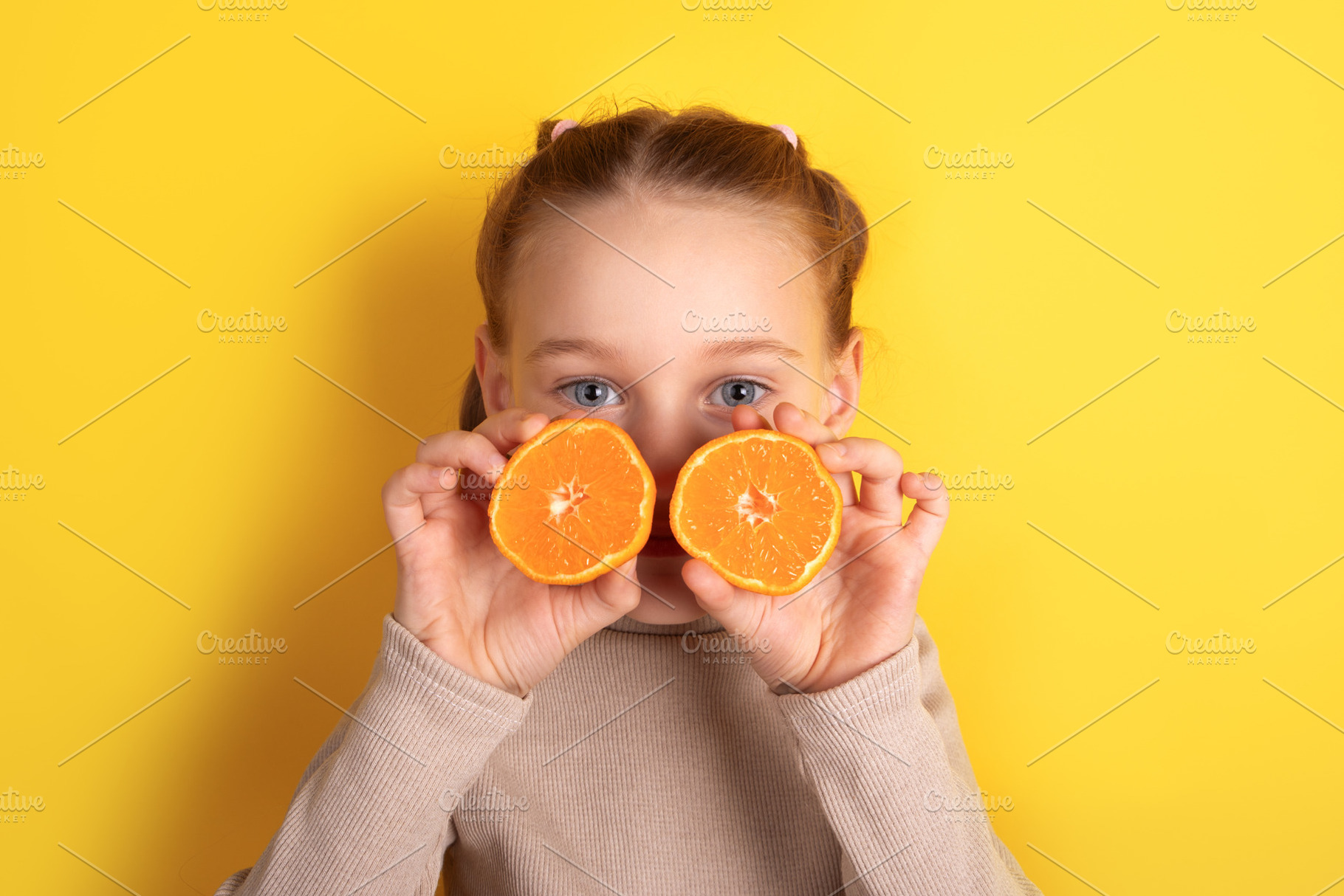 Smiling child holding two orange halves in front of eyes against, a Person Photo by Ales Munt