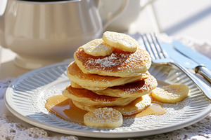 Pancakes stacked on a plate, topped with banana slices, powdered sugar, and map, a Photo by Studio ANNA