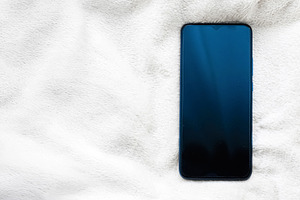 Smartphone resting on a soft white blanket, flat lay for comfort, technology, a, a Photo by Studio ANNA