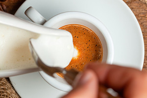 Barista pouring milk into espresso macchiato with croissant and coffee beans on, a Food & Drink Photo by Antonio Gravante Market