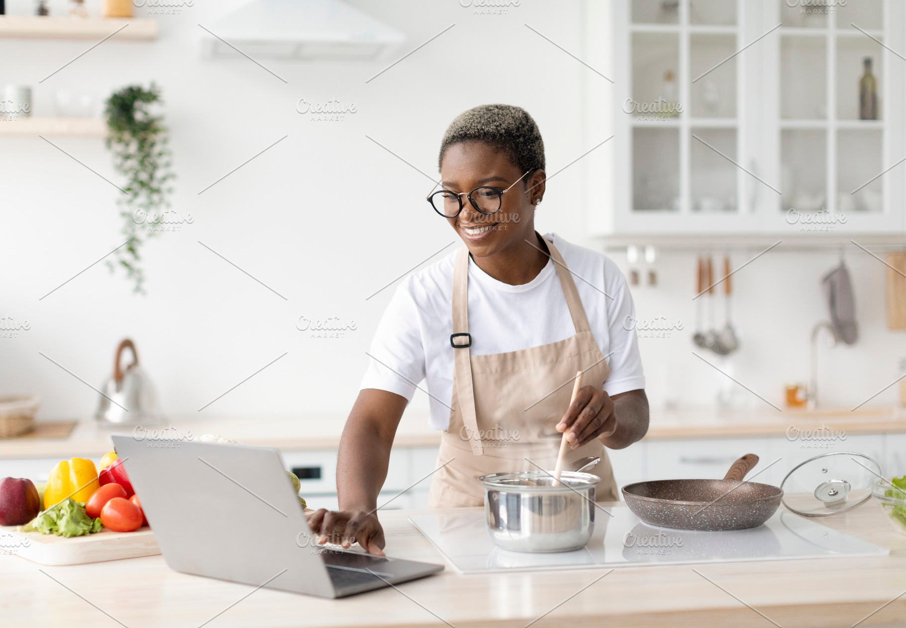 Smiling millennial african american female in glasses, apron cooking, watching, a Person Photo by Prostock-Studio