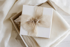 Elegant gift box with burlap ribbon bow on white textured fabric, a Photo by Studio ANNA