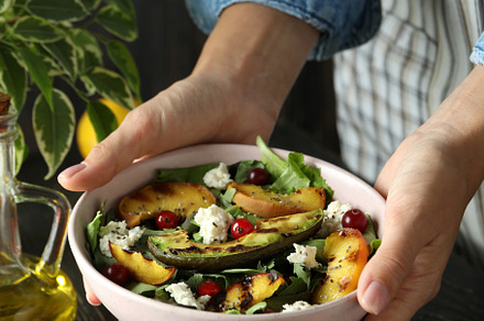 Woman in apron holds plate with salad with grilled peach, a Food & Drink Photo by AtlasStudio PRO