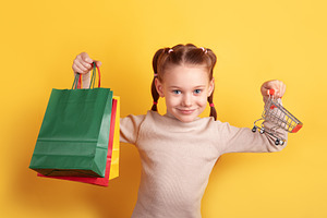 Smiling girl holding a shopping bag and miniature cart against a, a Person Photo by Ales Munt