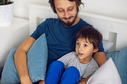 boy child and his father are sitting on the bed in the bedroom and laughing at, a Person Photo by SaulichPhoto