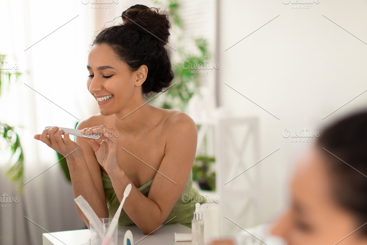 Positive millennial woman in towel filing nails near mirror after shower at bat, a Photo by Prostock-Studio (Photo 2 of 2)
