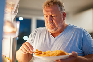 Man enjoying a late-night snack from the refrigerator, a Person Photo by AlyaAnd