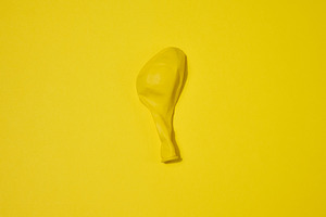 One yellow deflated balloon lies on a yellow background, an Abstract Photo by ndanko