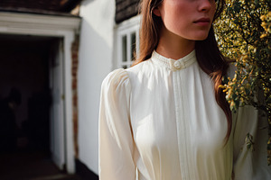 Woman wearing retro white blouse with high collar, standing in a, a Photo by Studio ANNA