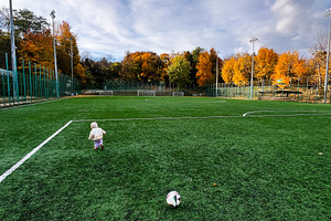A small child on a green autumn soccer field with a ball under a bright sky, a Photo by AS photostudio