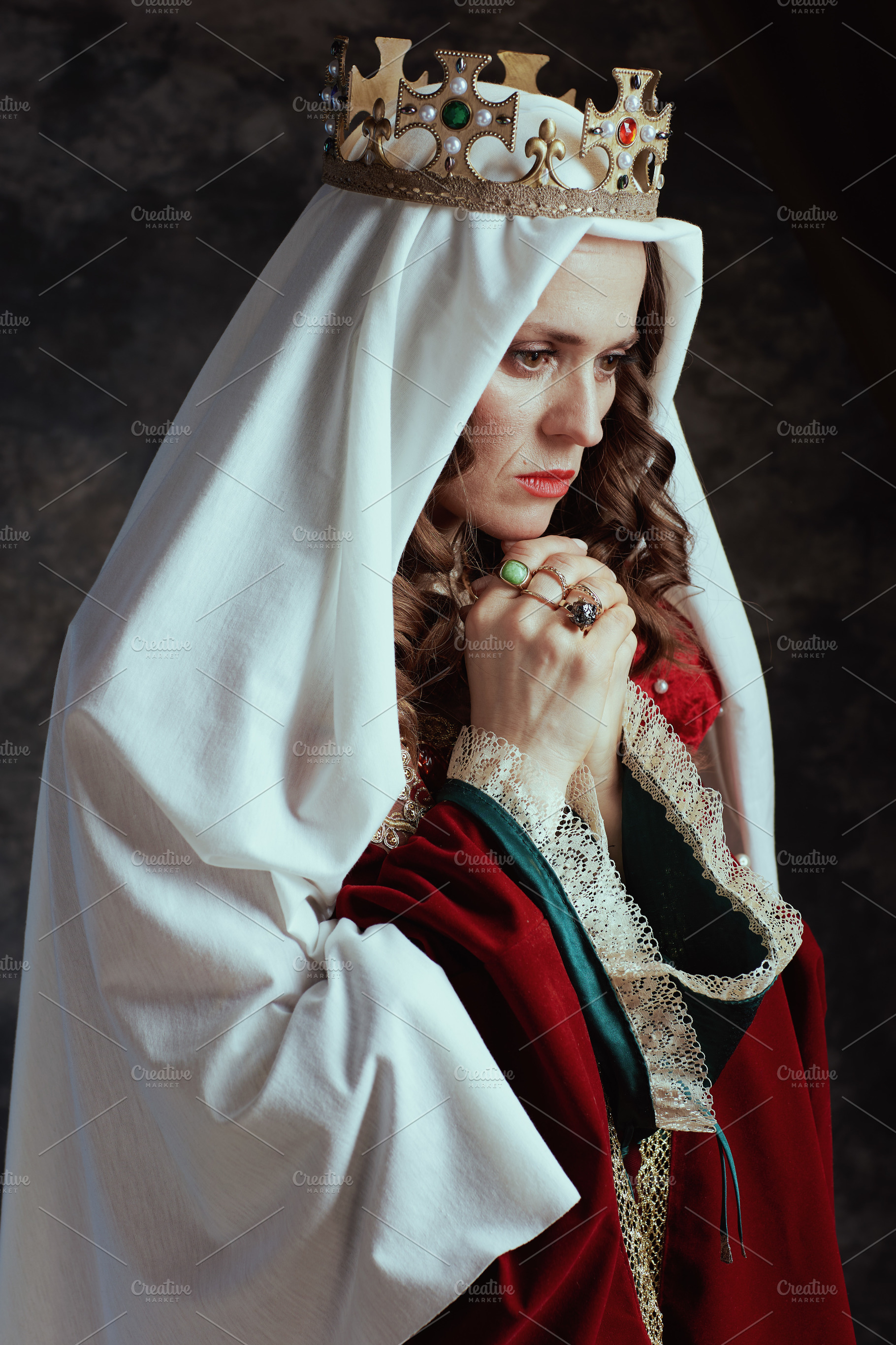 medieval queen in red dress with veil and crown praying, a Person Photo by Alliance Images