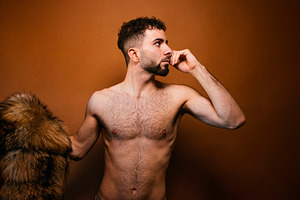 Young adult man posing with fur coat on shoulder in studio, a Photo by karrastock