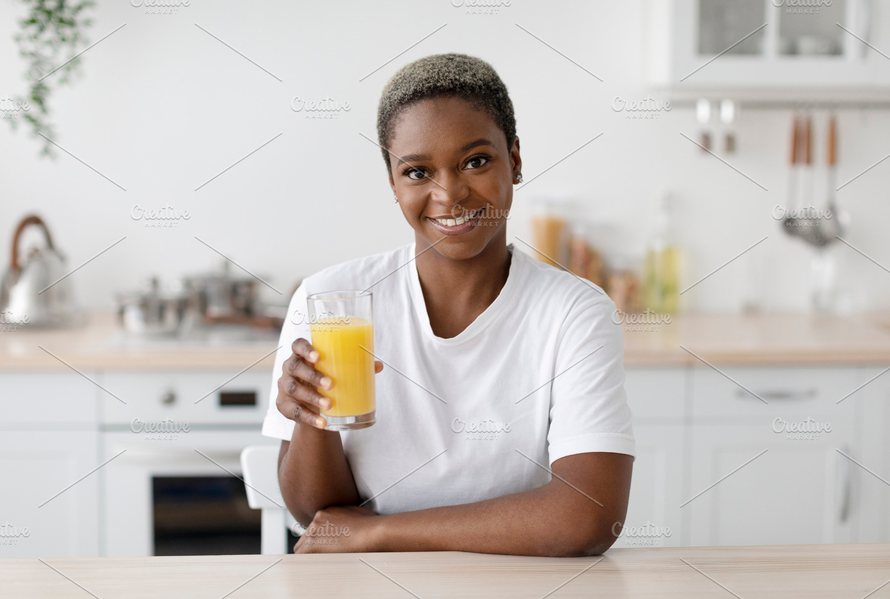 Smiling millennial african american woman in white t-shirt hold glass of organi, a Person Photo by Prostock-Studio