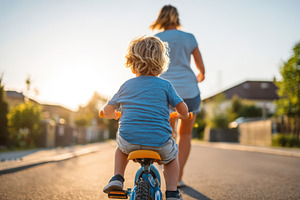 Child riding tricycle with woman jogging in background, a Person Photo by AlyaAnd
