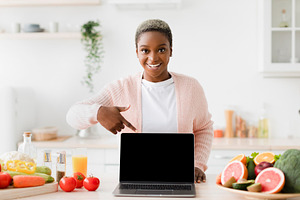 Happy glad excited young black female blogger points finger at pc with empty sc, a Person Photo by Prostock-Studio