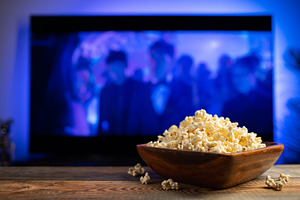 A wooden bowl of popcorn and remote control in the background the TV works. Eve, a Food & Drink Photo by Budarinphoto