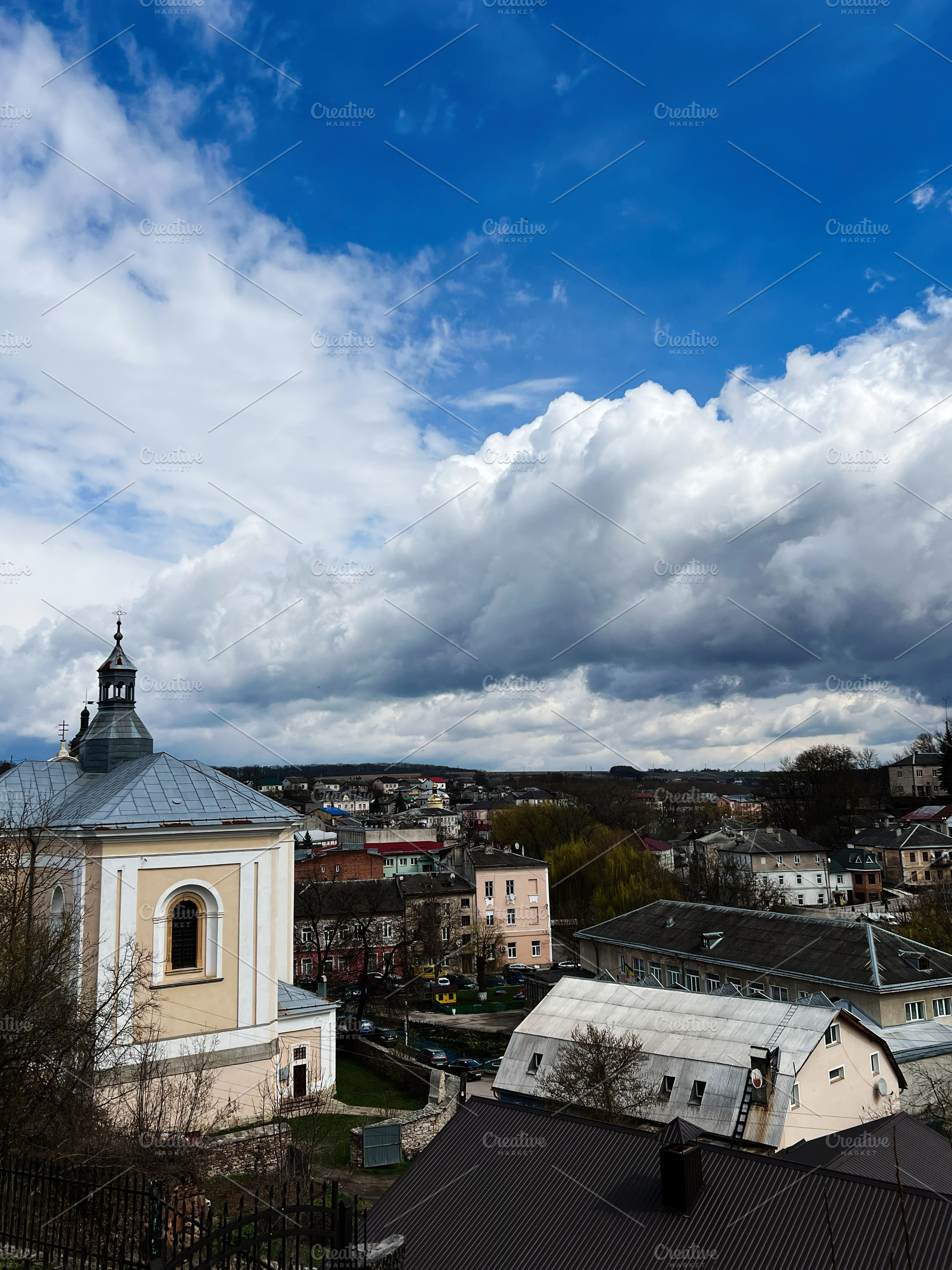 Elevated view of a serene townscape under a bright and expansive cloudy sky. Bu, a Photo by AS photostudio
