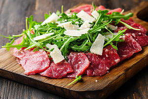 Beef carpaccio with arugula served on a wooden board in a rustic setting, a Food & Drink Photo by AlyaAnd