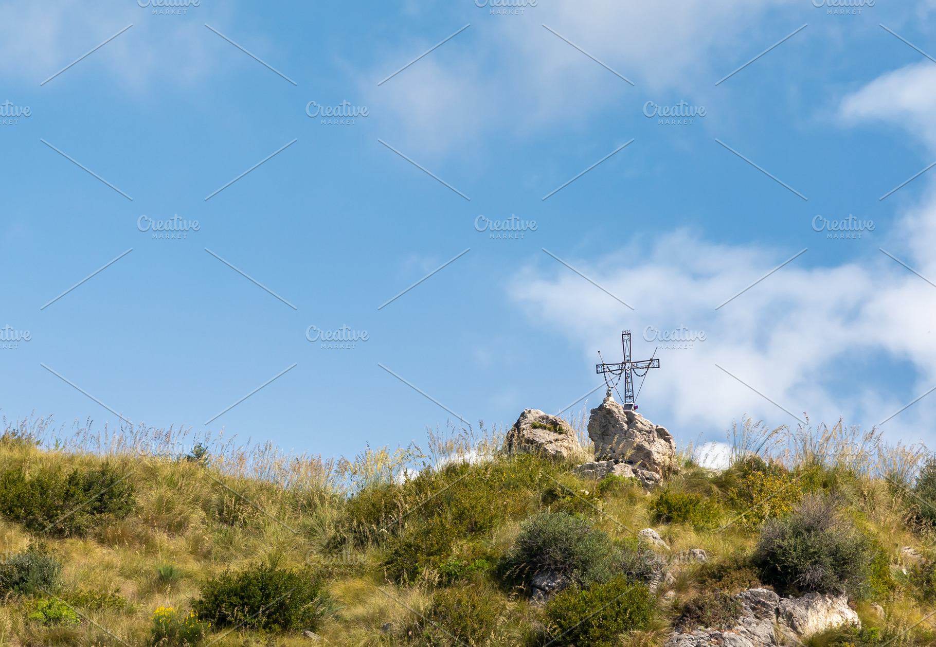 Large metal cross standing on a hilltop under blue sky, a Photo by Antonio Gravante Market