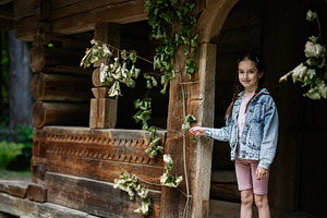 Young girl standing by traditional wooden structure surrounded by foliage outdo, a Person Photo by AS photostudio