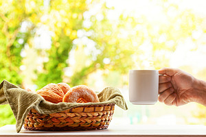Hand holding coffee mug with basket of pastries and autumn foliage in backgroun, a Food & Drink Photo by Antonio Gravante Market