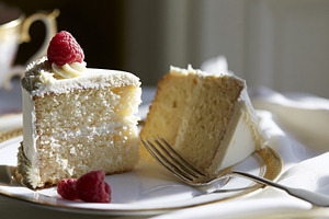 Vanilla cake slices with frosting and fresh raspberries on a golden rimmed plat, a Photo by Studio ANNA