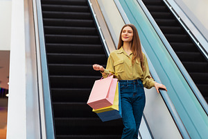 Lady Holding Shopping Bags Standing On Moving Stairs In Mall, a Photo by Prostock-Studio