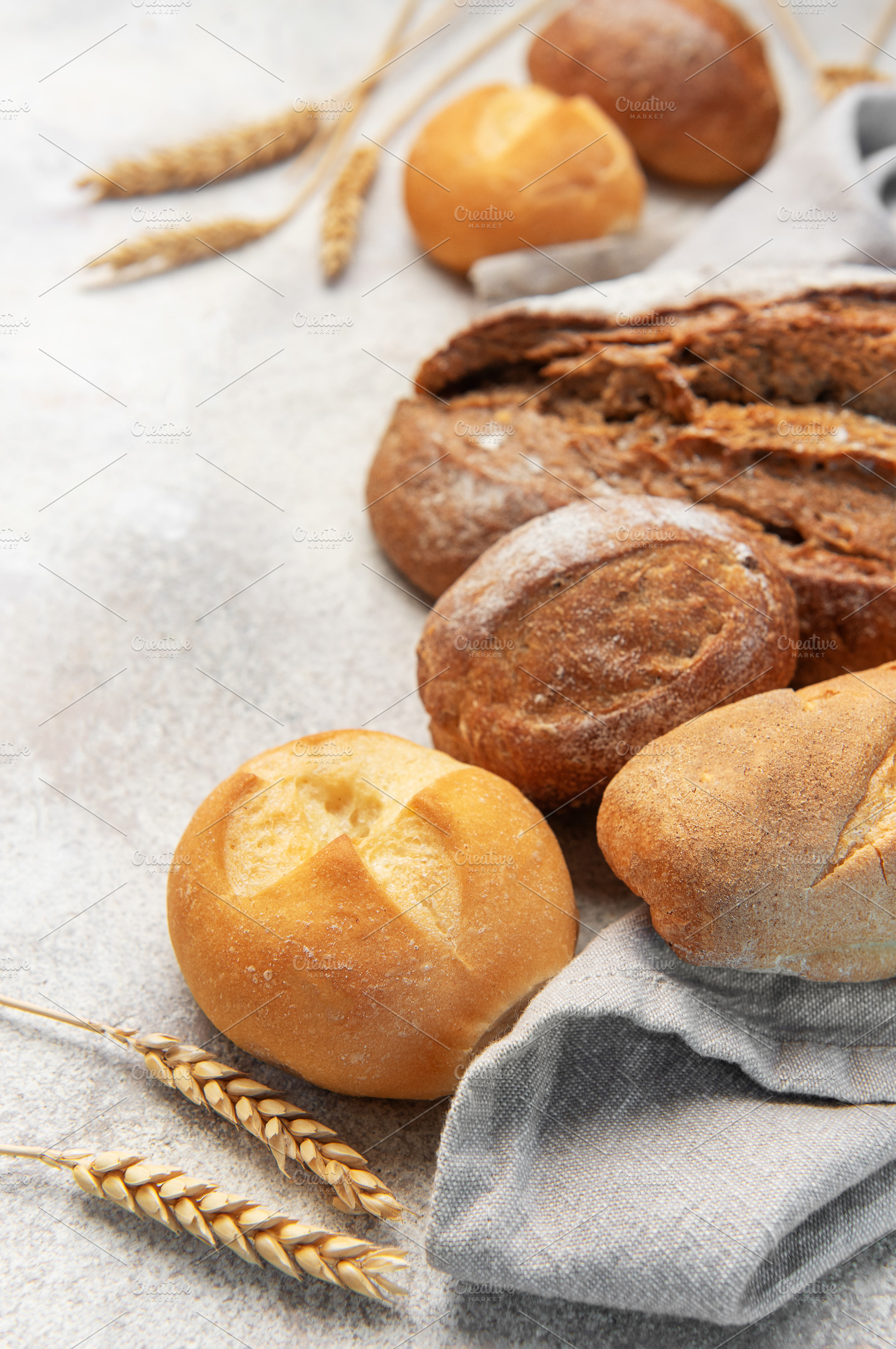 Fresh baked bread, rolls, wheat grain on concrete, a Food & Drink Photo by Olena Rudo