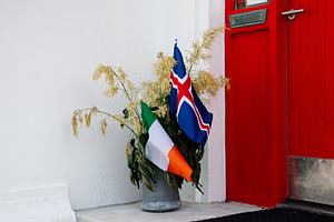 Irish and Icelandic flags displayed outside a vibrant red door in Akranes, Icel, a Photo by AS photostudio