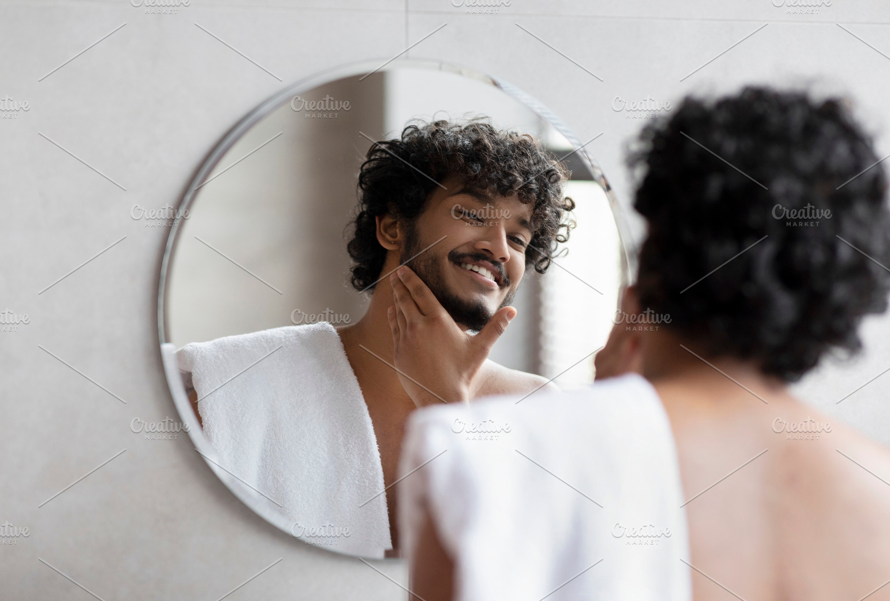 Handsome indian man looking in mirror in bathroom and touching beard, enjoying, a Person Photo by Prostock-Studio