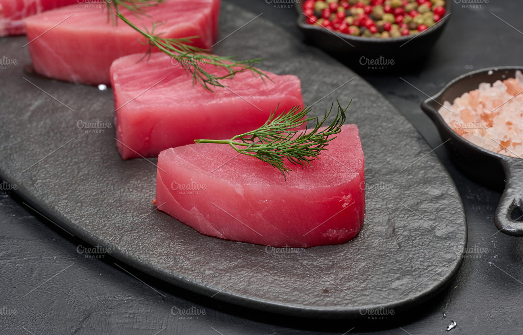 Raw piece of tuna with a sprig of dill on a black board, a Food & Drink Photo by ndanko