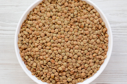 Organic green lentils in a white bowl on a white wooden surface,, a Food & Drink Photo by LiudmylaChuhunova