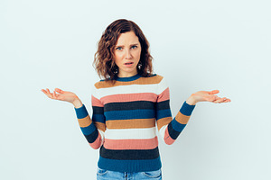 Young casual woman in disbelief shrugs shoulders