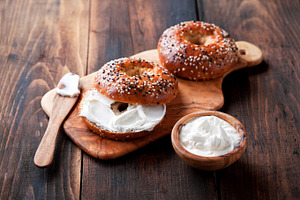 Whole grain bagels with cream cheese on wooden board