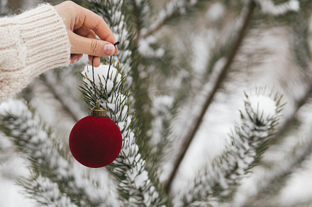 Hand in cozy sweater holding modern bauble on background of pine, a Holiday Photo by Sonjachni