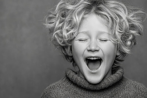 Child laughing with eyes closed in a cozy knit sweater studio portrait, a Photo by AS photostudio