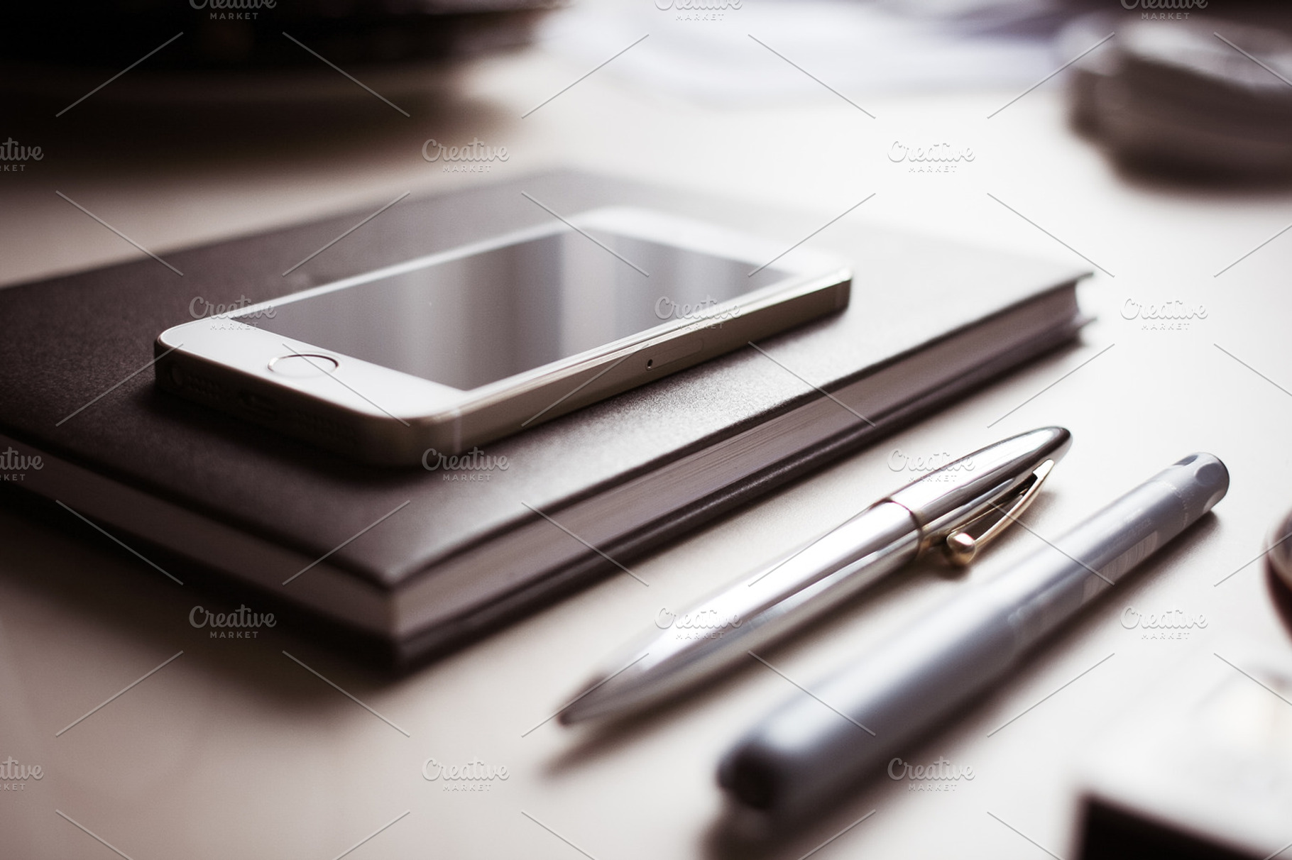 Iphone with pens & diary containing iphone, desk, and headphones