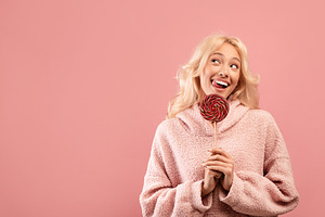 Sweet tooth concept. Playful lady holding candy on stick, looking aside at free, a Photo by Prostock-Studio
