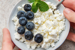 Hands holding a bowl of cottage cheese with blueberries and mint, a Food & Drink Photo by Olena Rudo