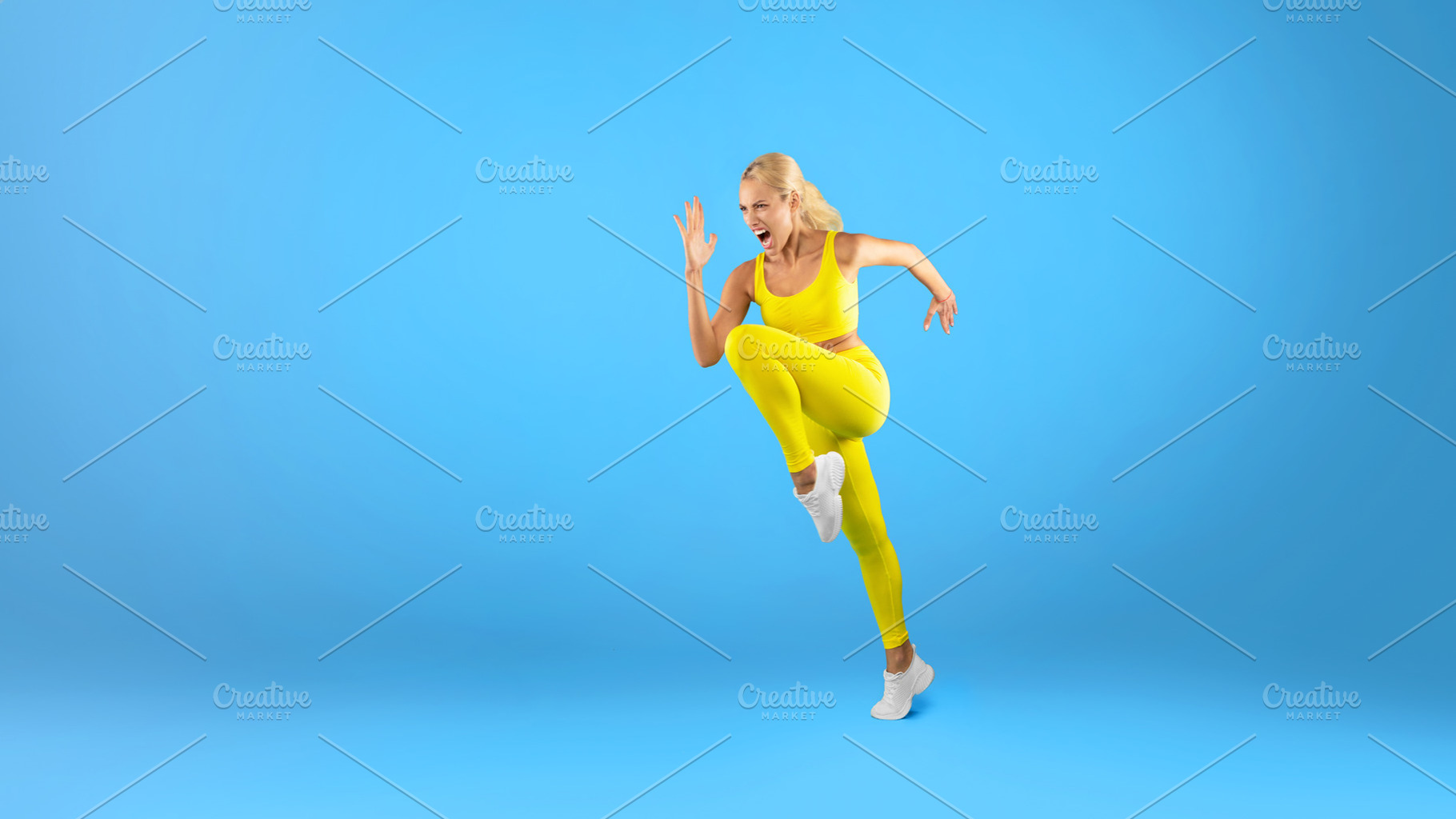 Fit woman running and screamng at blue studio background, a Photo by Prostock-Studio