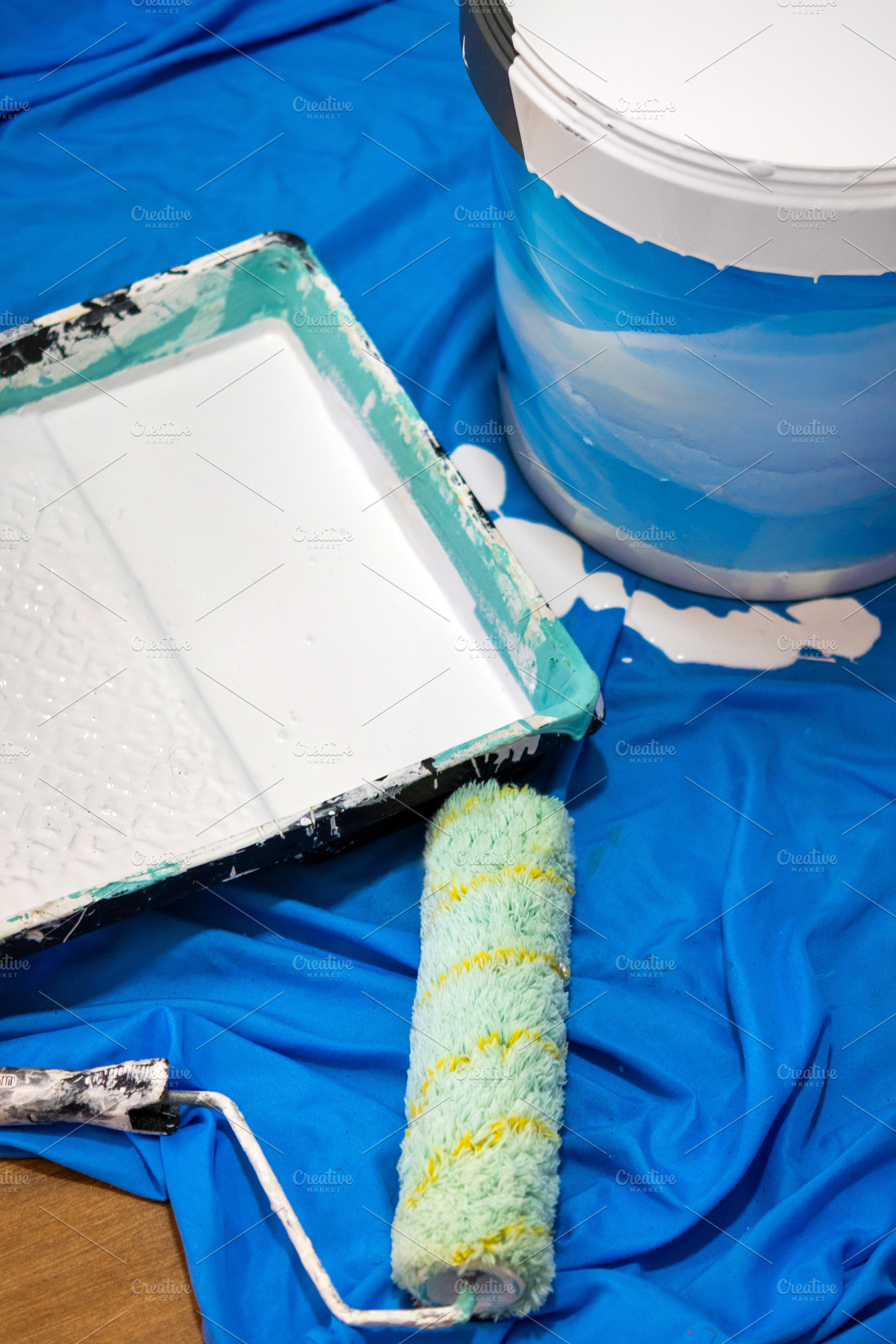 Paint roller, tray and bucket with white paint on blue protective sheet, an Industrial Photo by etorres69