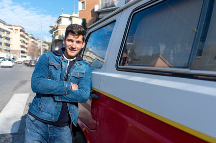 A Happy young man leaning at the retro mini van