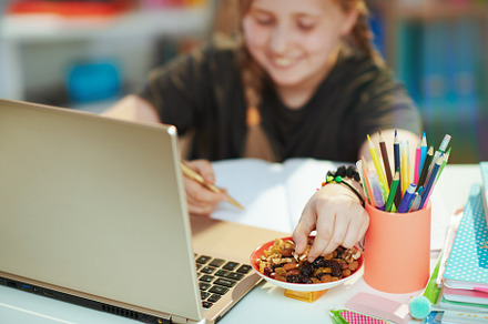 Smiling girl having online education and eating healthy snack, a School & Education Photo by Alliance Images