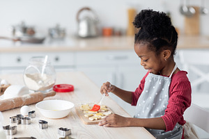 Adorable little black girl making cookies, side view, a Photo by Prostock-Studio