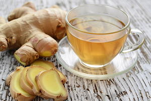 Glass cup of ginger tea with sliced ginger root on white wooden background, a Food & Drink Photo by AlyaAnd